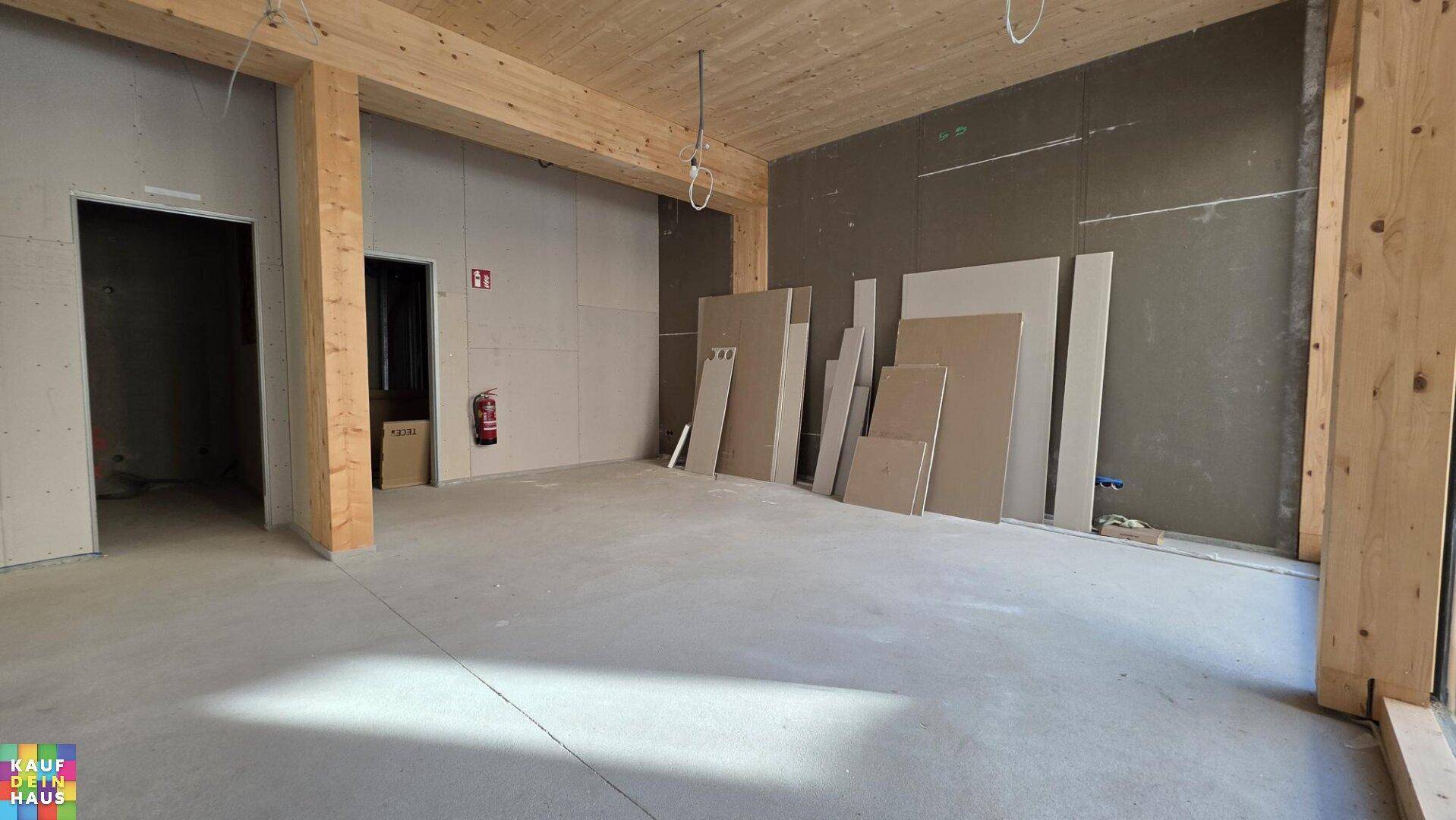 Unfertiger Innenraum mit Holzbalken, Trockenbauwänden und Baumaterialien, bereit für den Ausbau.
