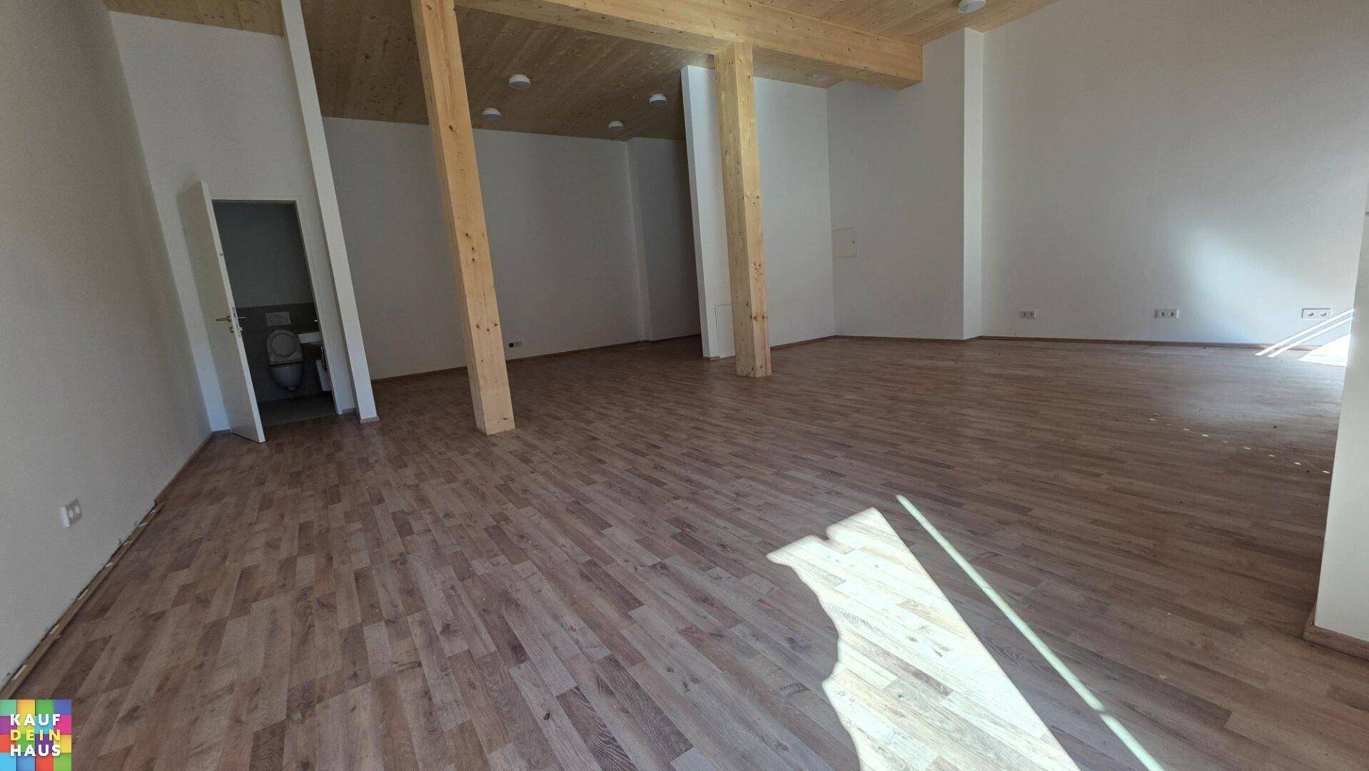 Großer, heller Raum mit Holzboden und sichtbaren Holzträgern, ideal für verschiedene Nutzungen.