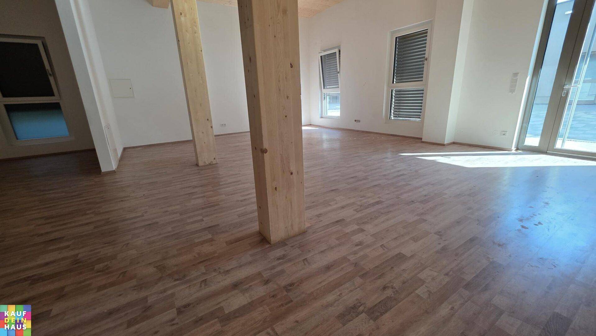 Heller Innenraum mit Holzboden, großen Fenstern und Zugang zu einem Außenbereich.