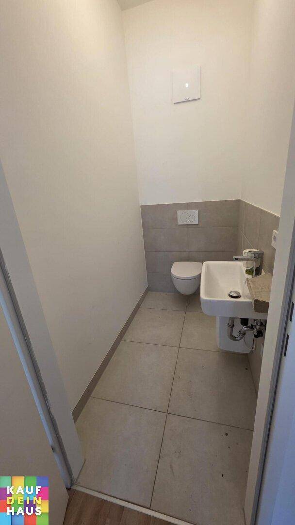 Kompakte Gästetoilette mit wandhängendem WC, Waschbecken und modernen Fliesen.