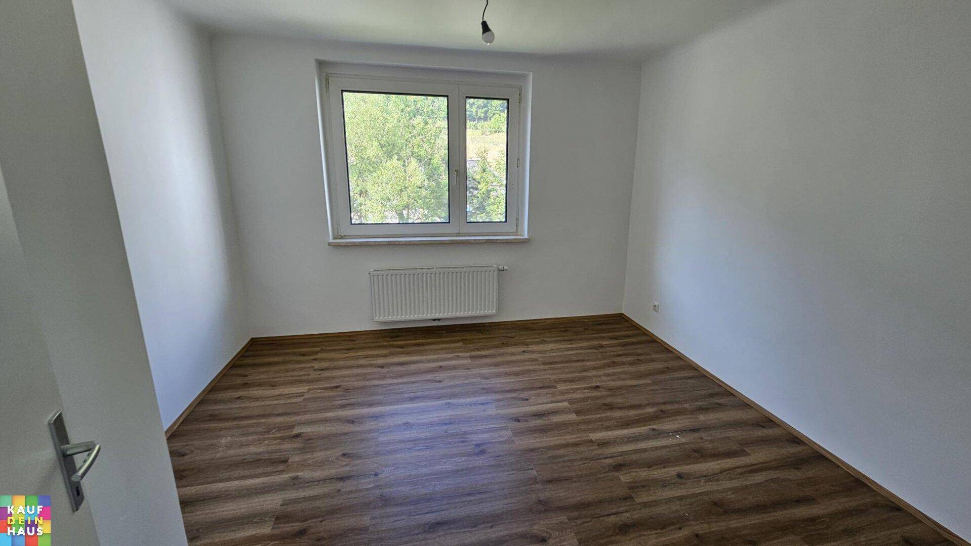 Helles Schlafzimmer mit Laminatboden und Fenster mit Blick ins Grüne.