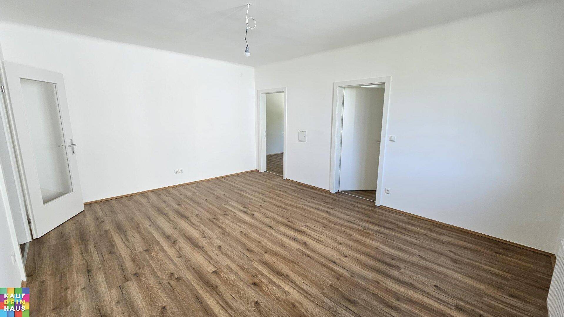 Geräumiges, unmöbliertes Wohnzimmer mit Laminatboden und weiß gestrichenen Wänden.