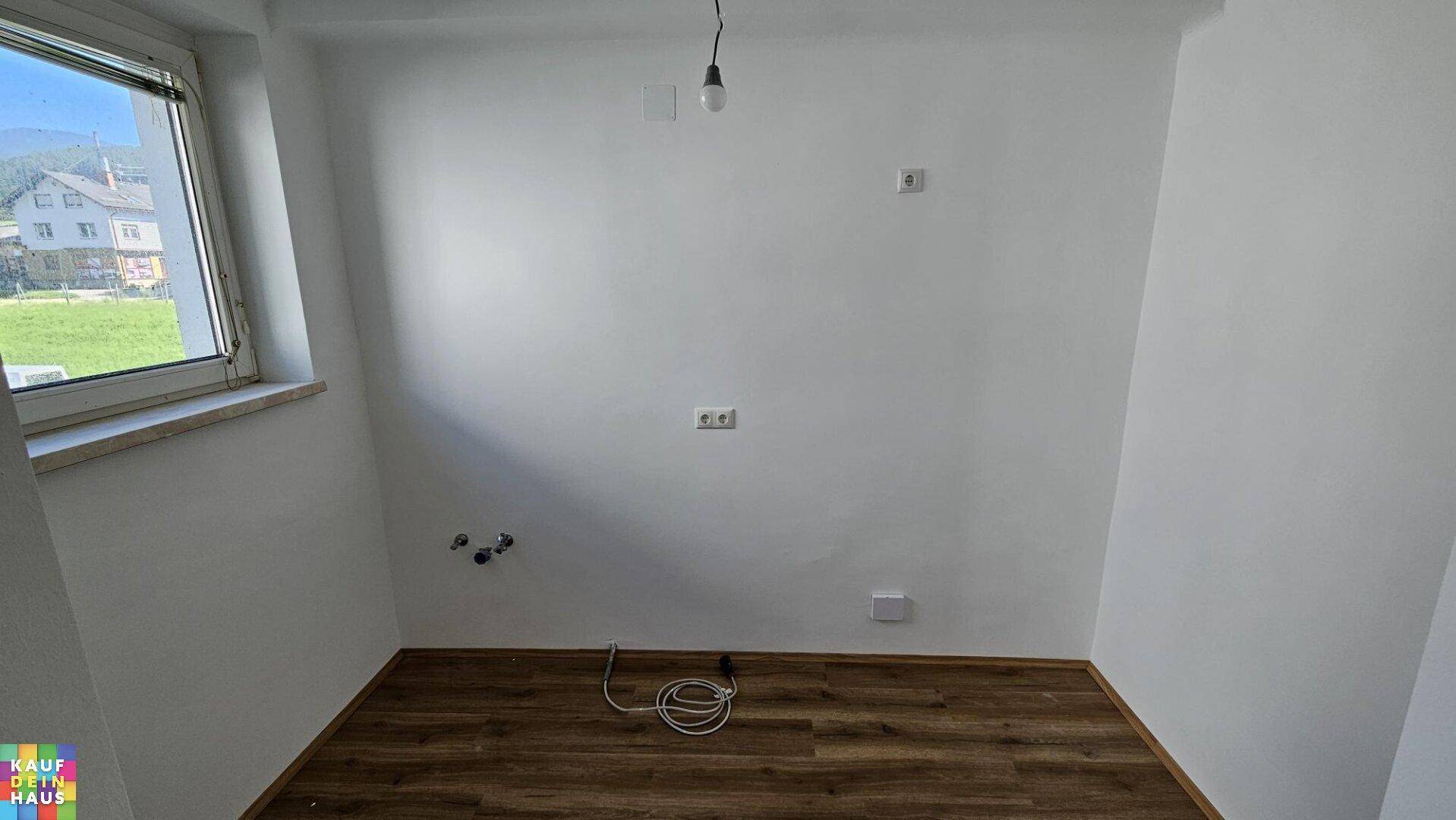 Leerer Küchenraum mit Anschlüssen für Spüle und Geräte sowie Blick ins Grüne.