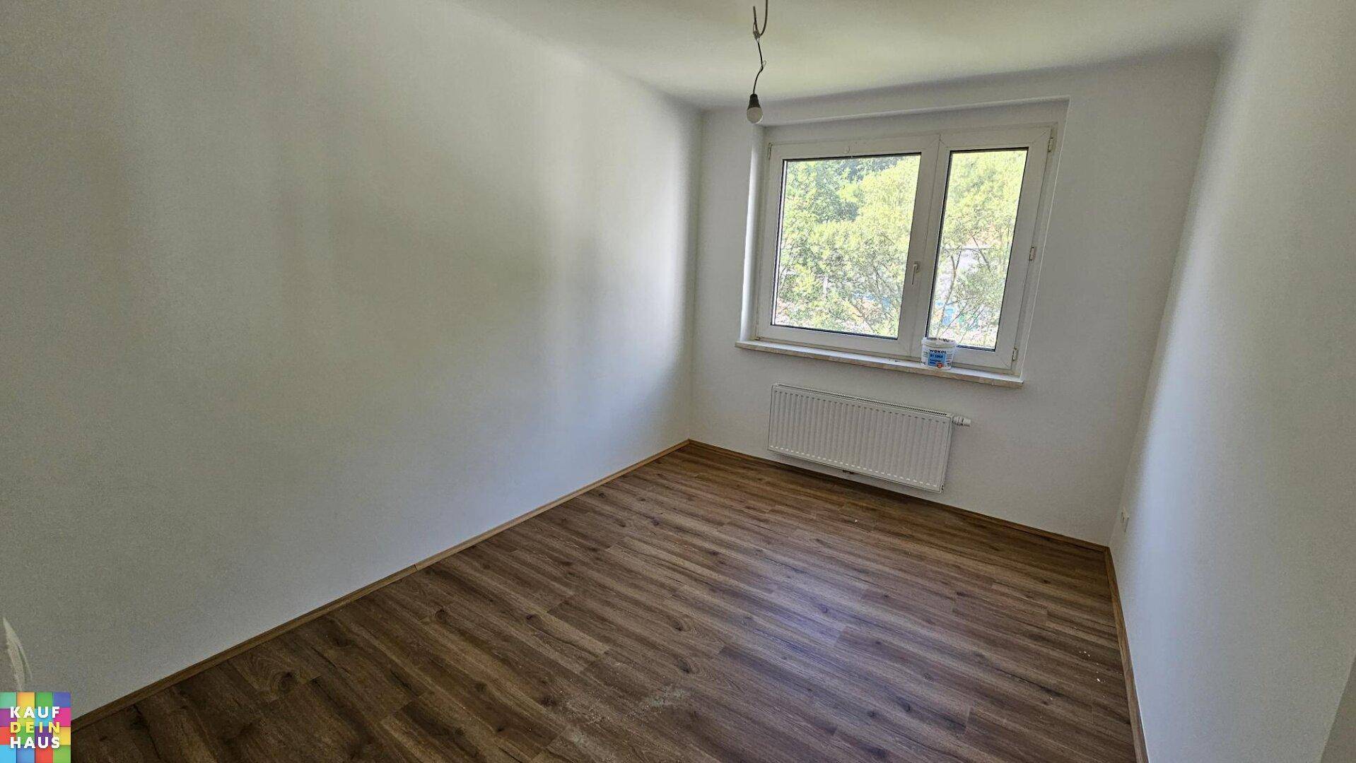 Unmöbliertes Schlafzimmer mit Laminatboden und einem Fenster, das viel Tageslicht hereinlässt.