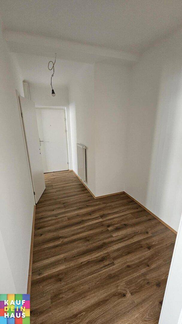 Heller Flur mit Laminatboden und weiß gestrichenen Wänden, der zu weiteren Räumen führt.