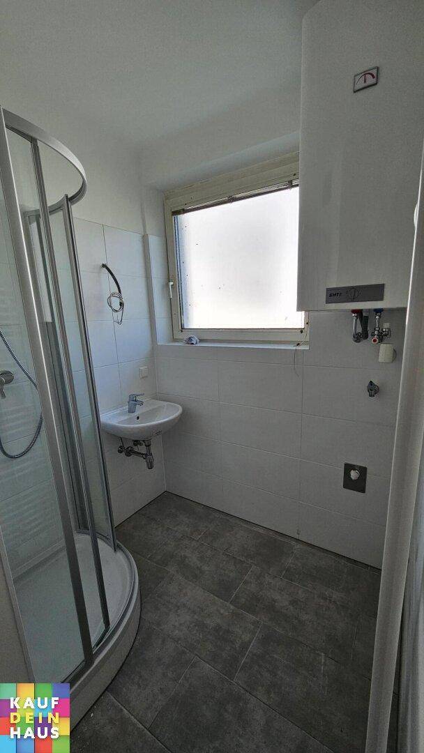 Badezimmer mit Duschkabine, Waschbecken und Fenster für natürliche Belüftung.