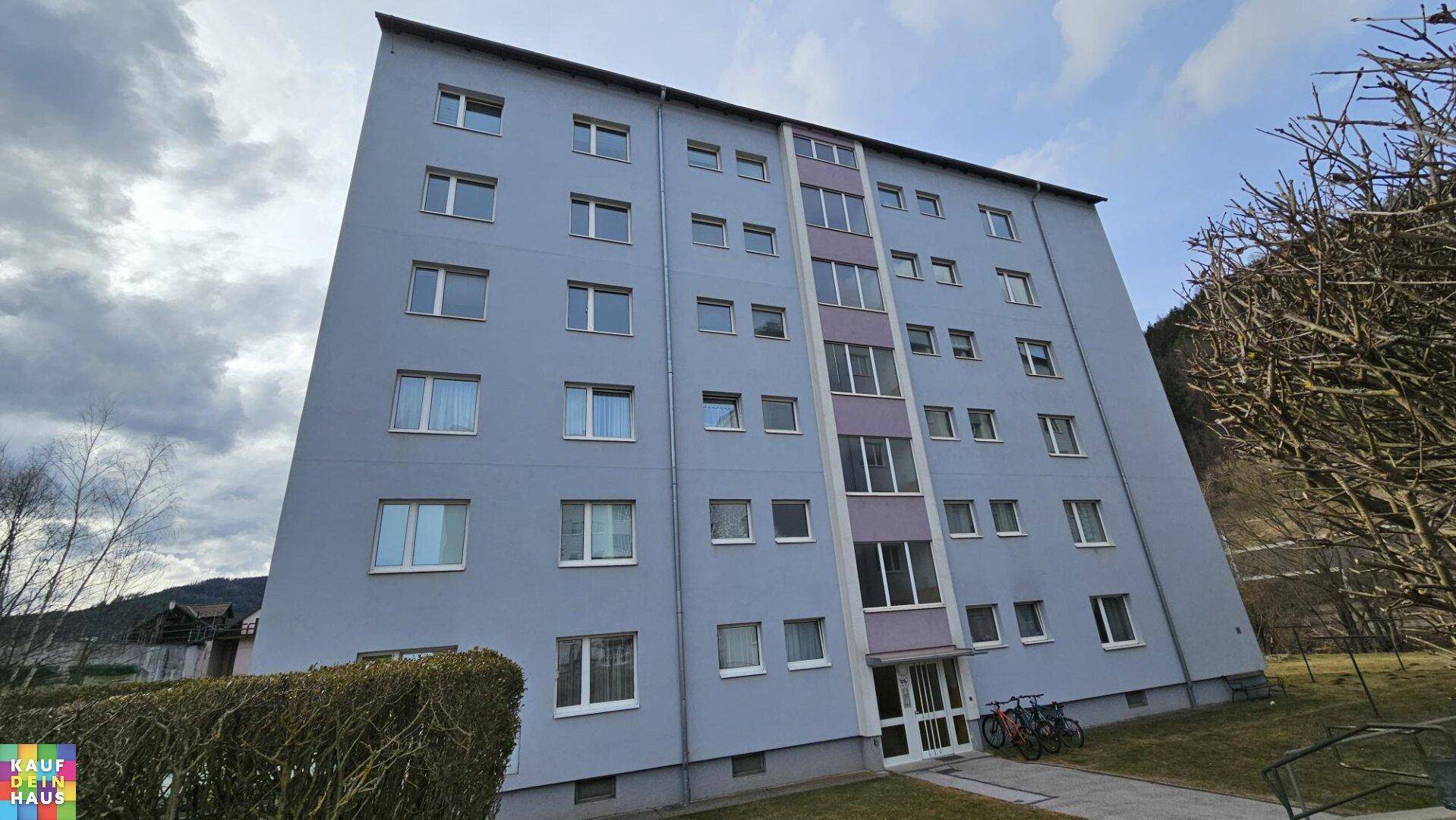 Mehrstöckiges Wohngebäude mit blauer Fassade und vielen Fenstern unter bewölktem Himmel.