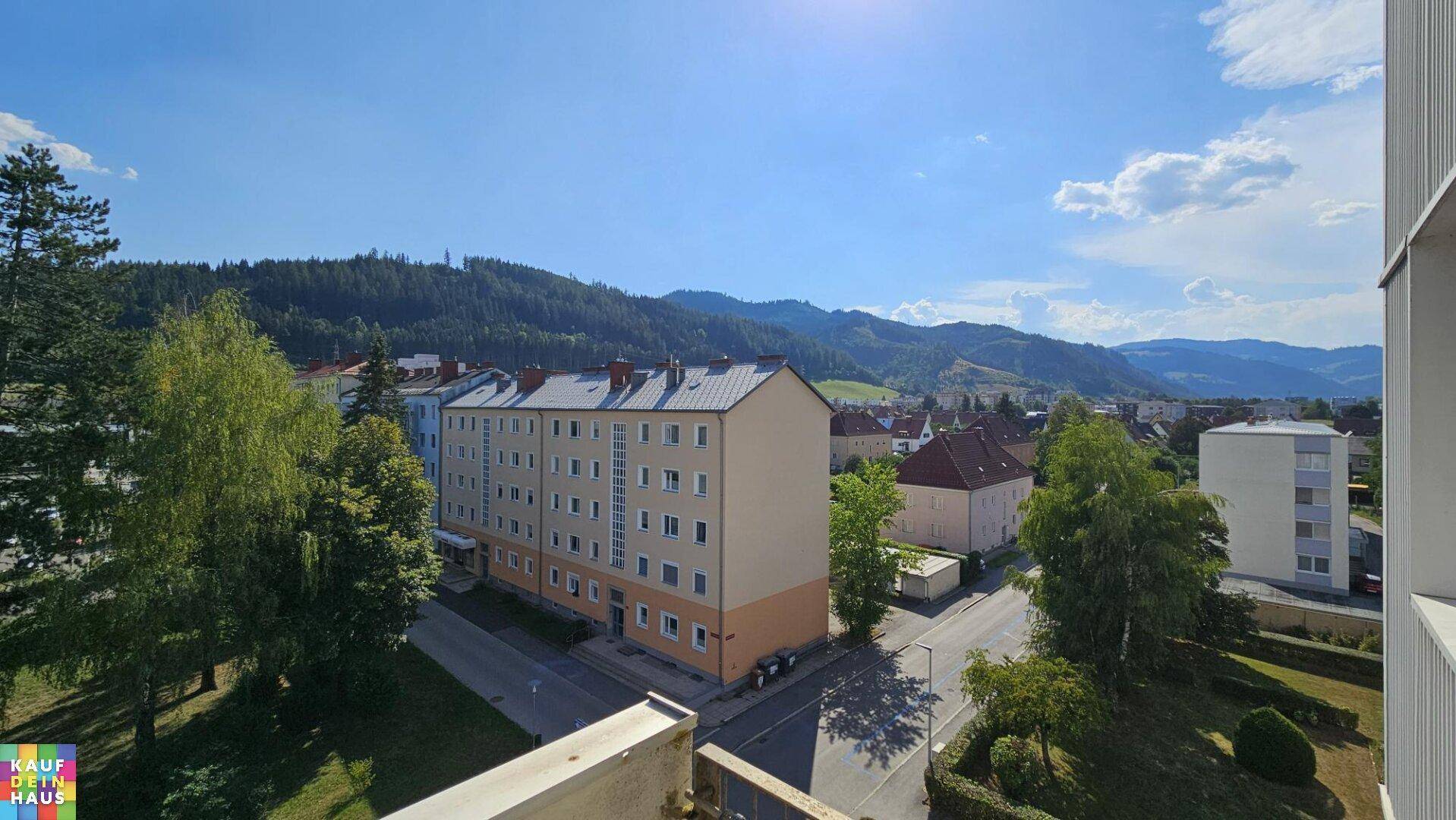Weitblick über die umliegende Wohngegend mit grünen Hügeln und Bergen im Hintergrund.