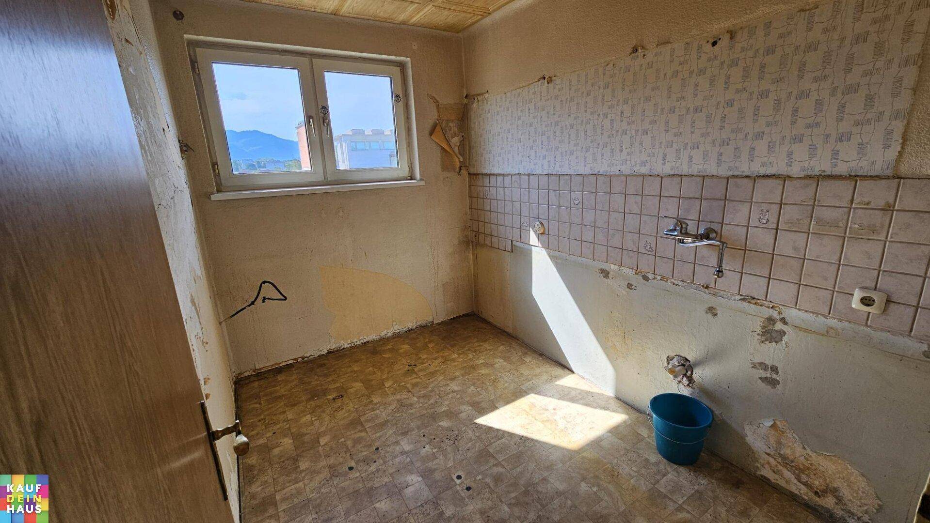 Sanierungsbedürftige Küche mit alten Fliesen und Fenster, bietet Potenzial für eine moderne Gestaltung.
