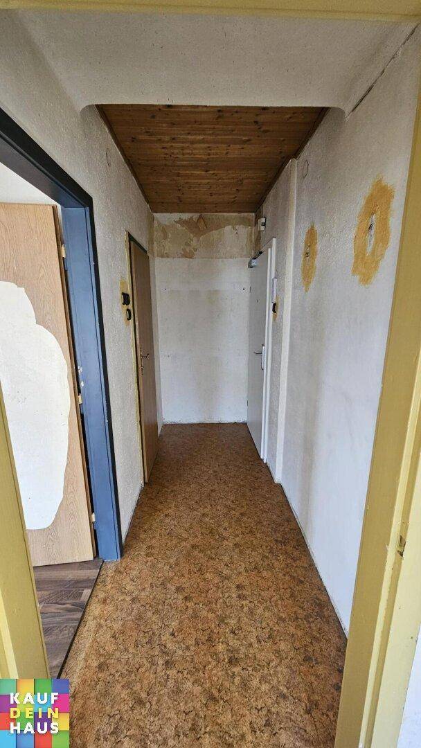 Flur mit Teppichboden und Holzdecke, der zu verschiedenen Zimmern der Wohnung führt.