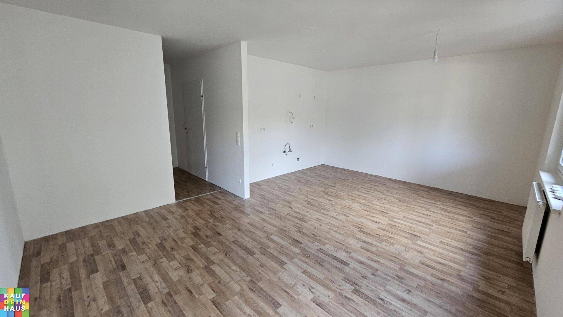 Geräumiges, leeres Wohnzimmer mit hellem Laminatboden und weißen Wänden.