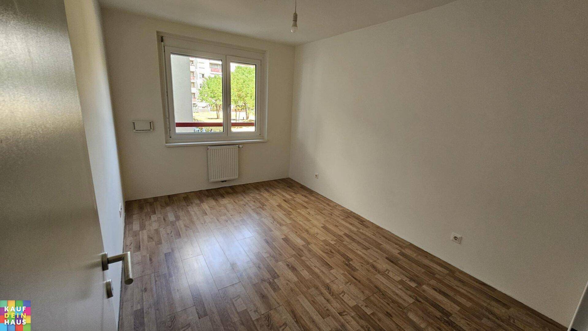 Helles, leeres Schlafzimmer mit Laminatboden und Fenster zum Innenhof.