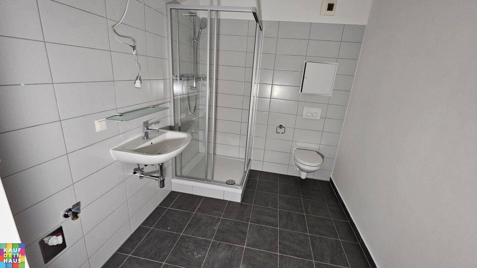 Modernes Badezimmer mit Duschkabine, Waschbecken und grauen Fliesen.