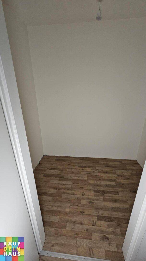 Kleiner, leerer Raum mit schrägen Wänden und Laminatboden, möglicherweise ein Abstellraum.