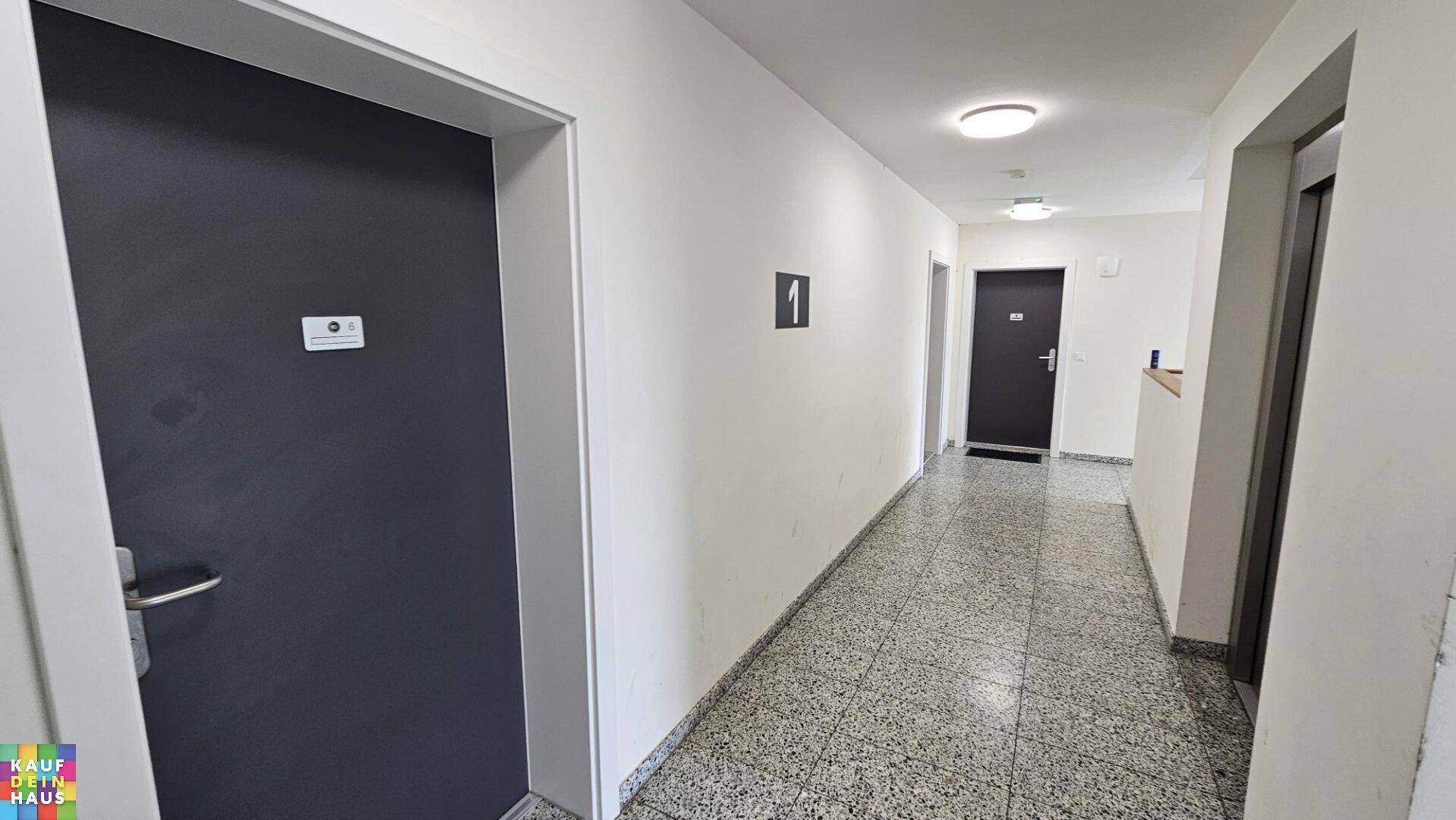 Gemeinschaftlicher Flur mit Terrazzoboden und mehreren Wohnungstüren.