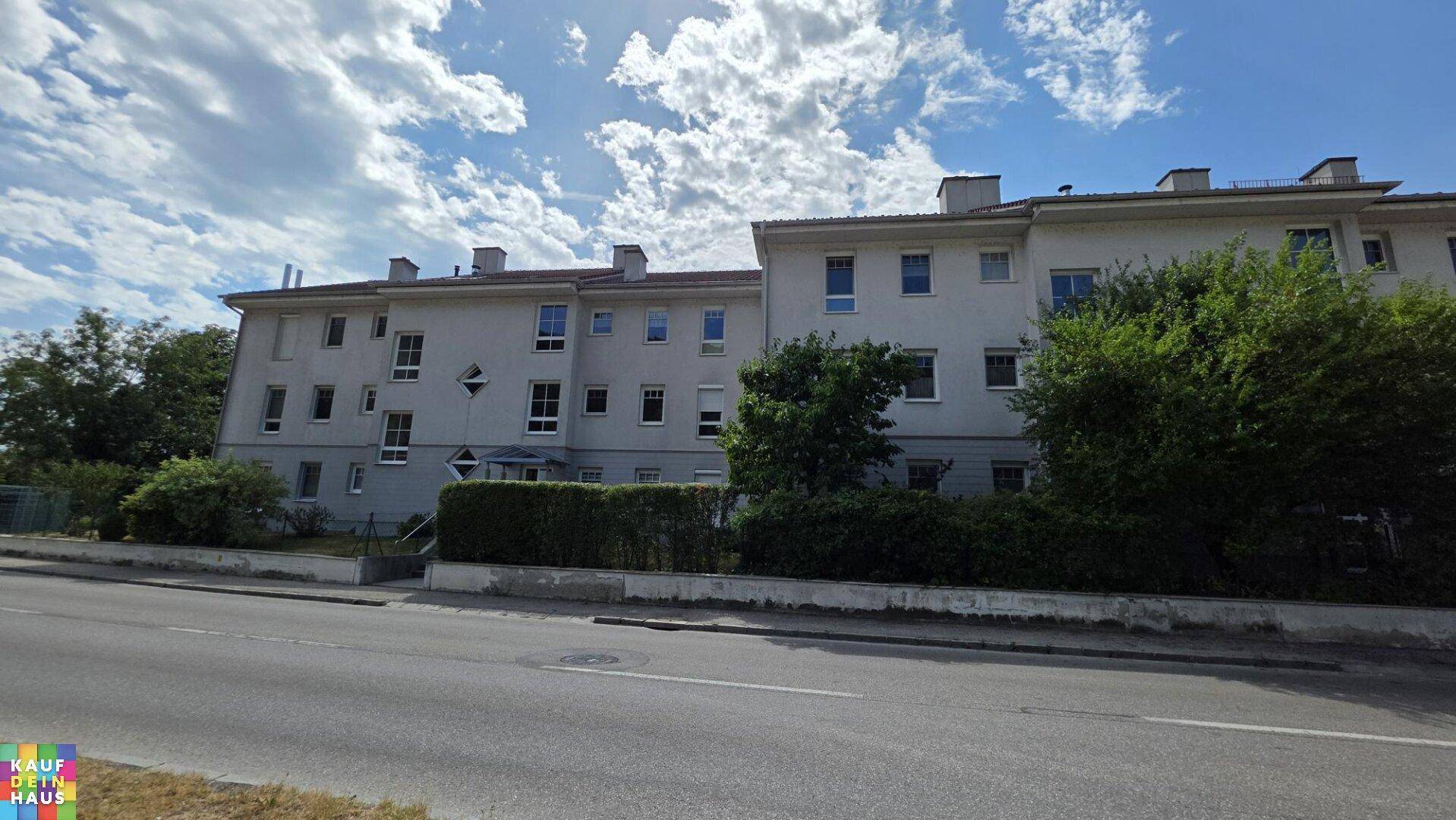 Ansicht eines Mehrfamilienhauses mit mehreren Fenstern und gepflegter Hecke im Vordergrund.
