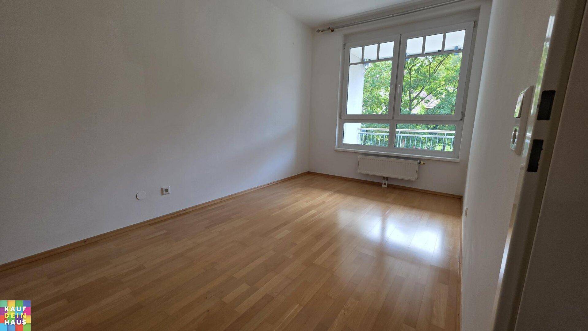 Geräumiges Zimmer mit Laminatboden und großem Fenster, bietet viel Tageslicht und Grünblick.