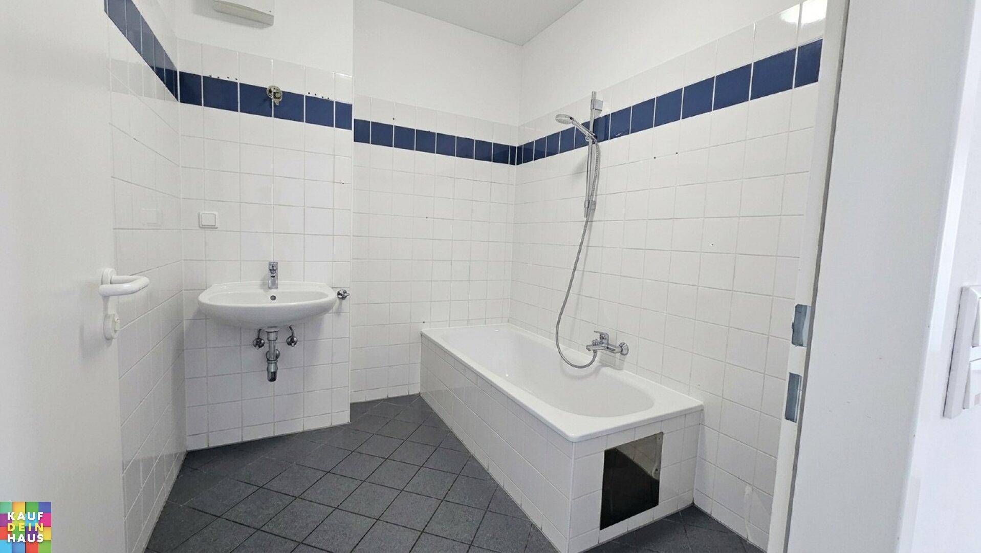 Badezimmer mit Badewanne, Waschbecken und weißen Fliesen, akzentuiert durch blaue Bordüren.
