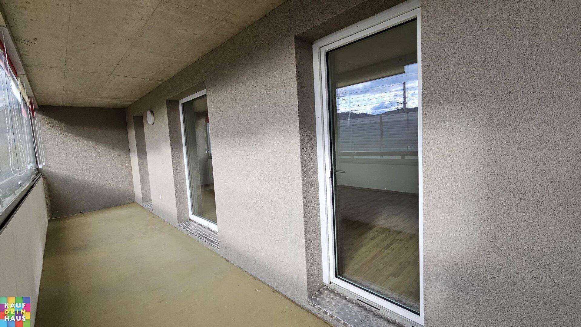 Überdachte Loggia mit Betonwänden und großen Fenstern, die den Innenraum mit dem Außenbereich verbinden.