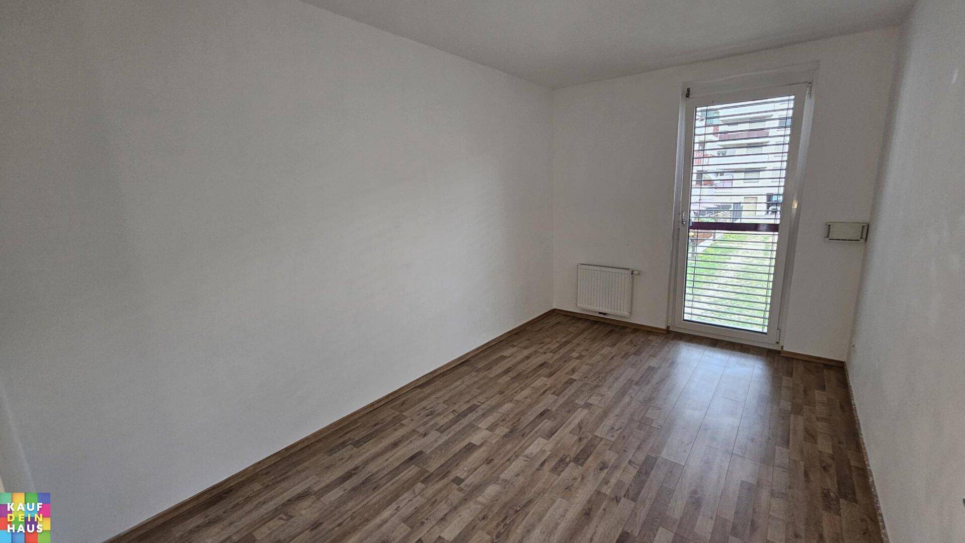 Helles Schlafzimmer mit Holzboden und einer Fenstertür, die Zugang zu einem kleinen Außenbereich bietet.