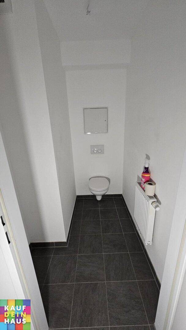 Separates WC mit dunklen Bodenfliesen und einer wandhängenden Toilette, praktisch und platzsparend.