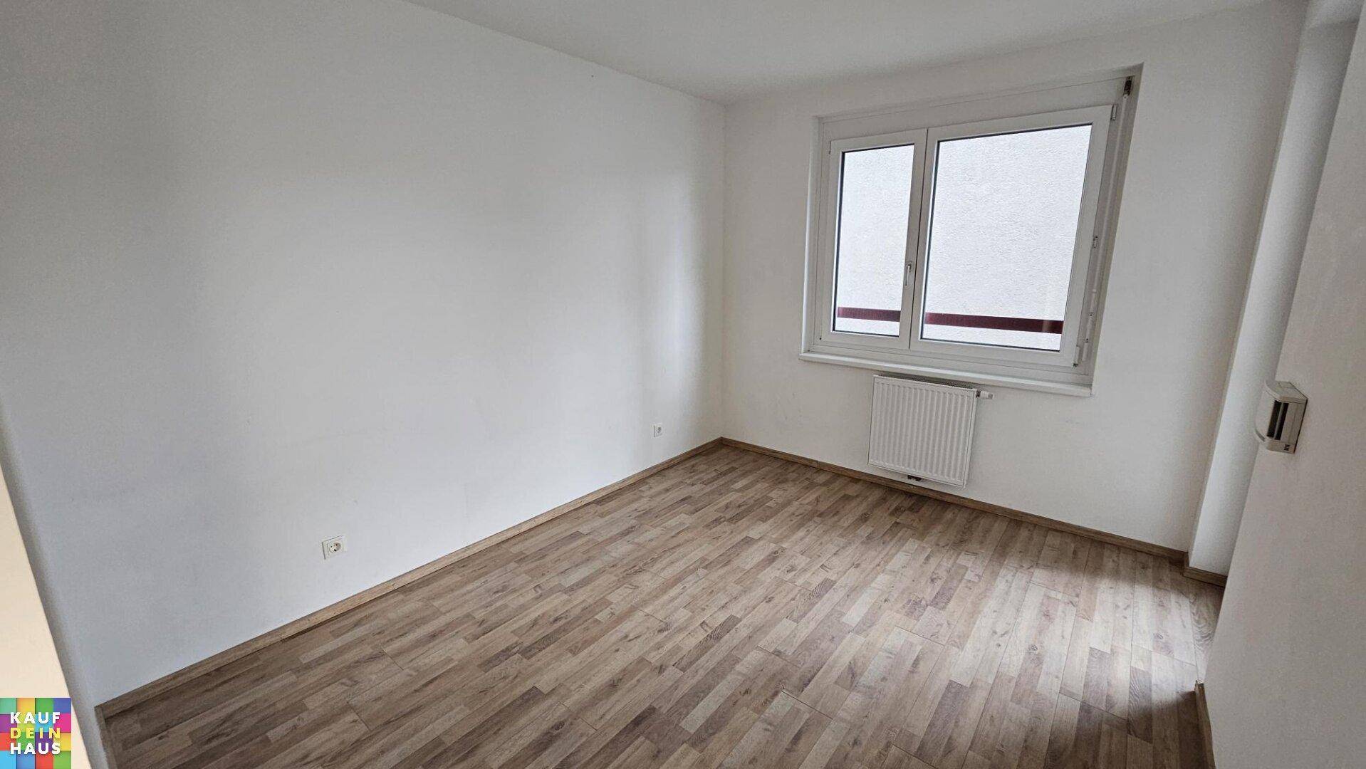 Helles Schlafzimmer mit Holzboden, großem Fenster und Heizkörper.
