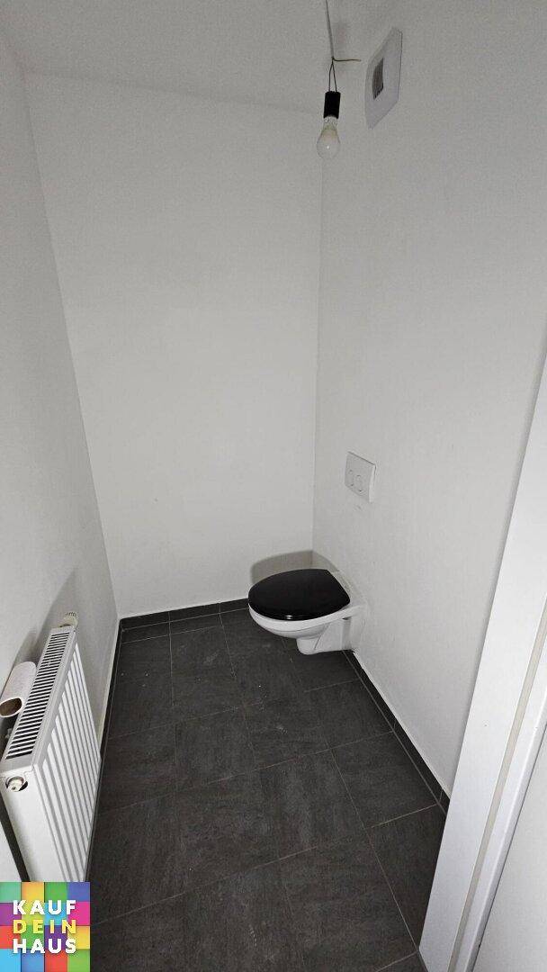 Separates WC mit Toilette, Heizkörper und dunklen Bodenfliesen.
