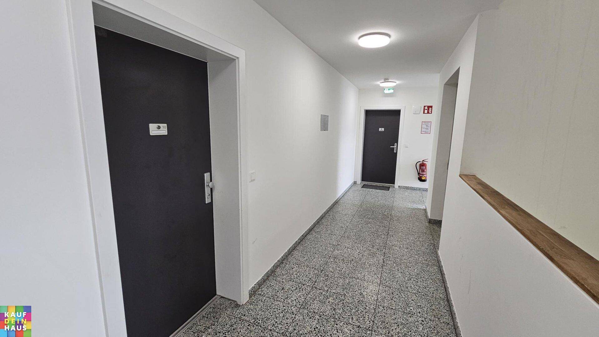 Gemeinschaftlicher Flur im Gebäude mit Terrazzoboden und mehreren Wohnungstüren.