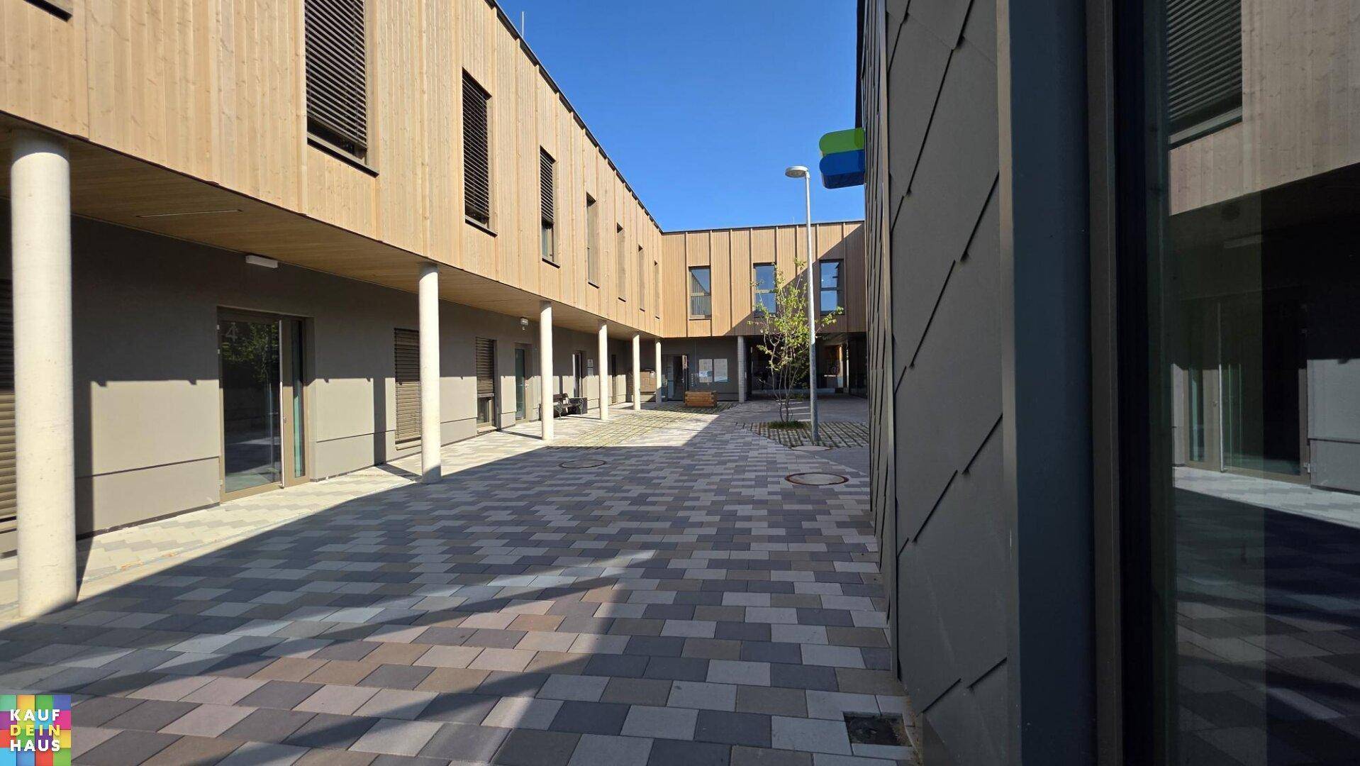 Blick auf den gepflasterten Innenhof umgeben von modernen Gebäuden mit Holzverkleidung.