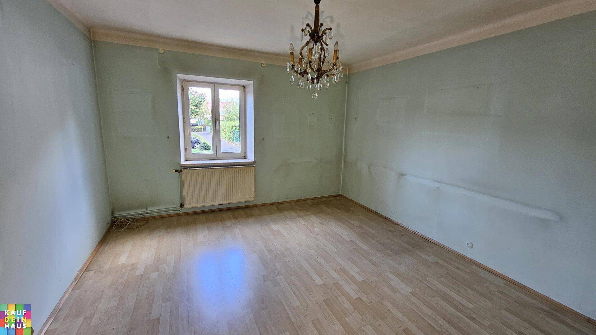 Helles Zimmer mit Laminatboden, Kronleuchter und einem Fenster mit Blick ins Grüne.
