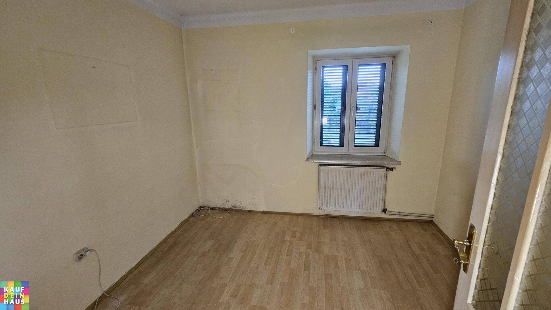 Kleines Zimmer mit Laminatboden und einem Fenster mit Jalousien, das renovierungsbedürftig ist.