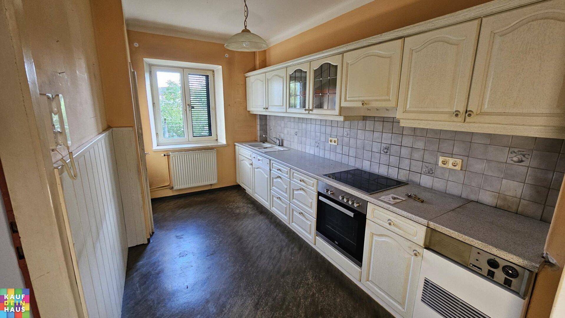 Funktionale Einbauküche mit hellen Schränken, Fliesenrückwand und integrierten Elektrogeräten.