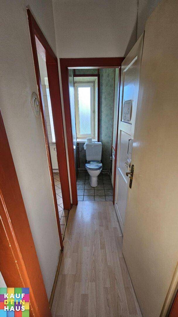 Schmaler Flur mit Laminatboden, der zu einem separaten WC mit kleinem Fenster führt.