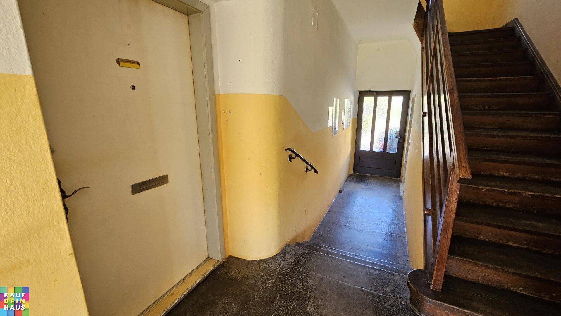Eingangsbereich mit Holztreppe und gelb gestrichenen Wänden, führt zu den oberen Etagen.