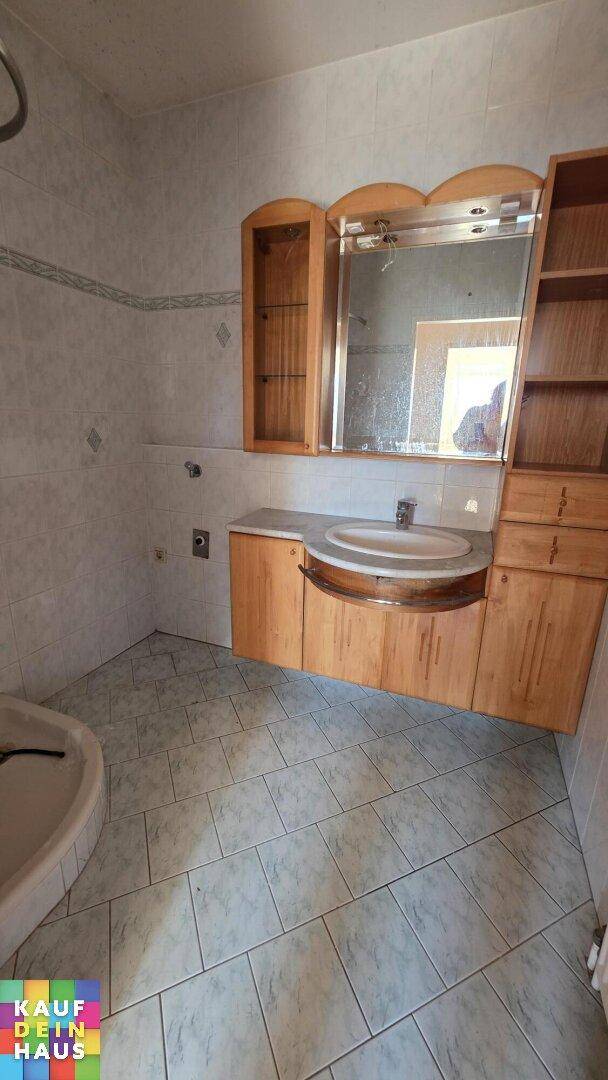 Badezimmer mit hellgrauen Fliesen, Holzwaschtisch, Spiegelschrank und einem Bidet.