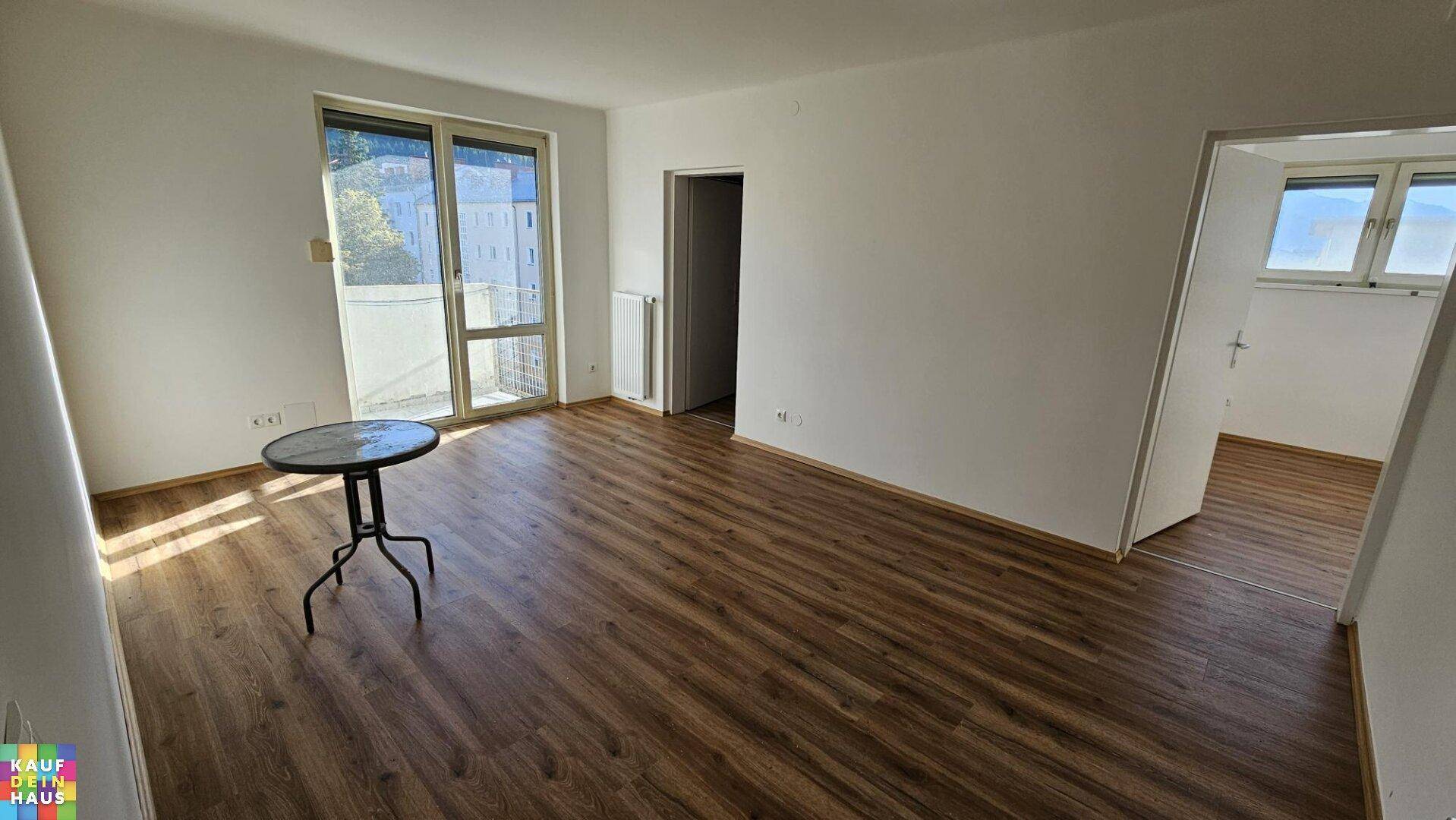 Helles Wohnzimmer mit Laminatboden und Zugang zu einem Balkon oder einer Terrasse.