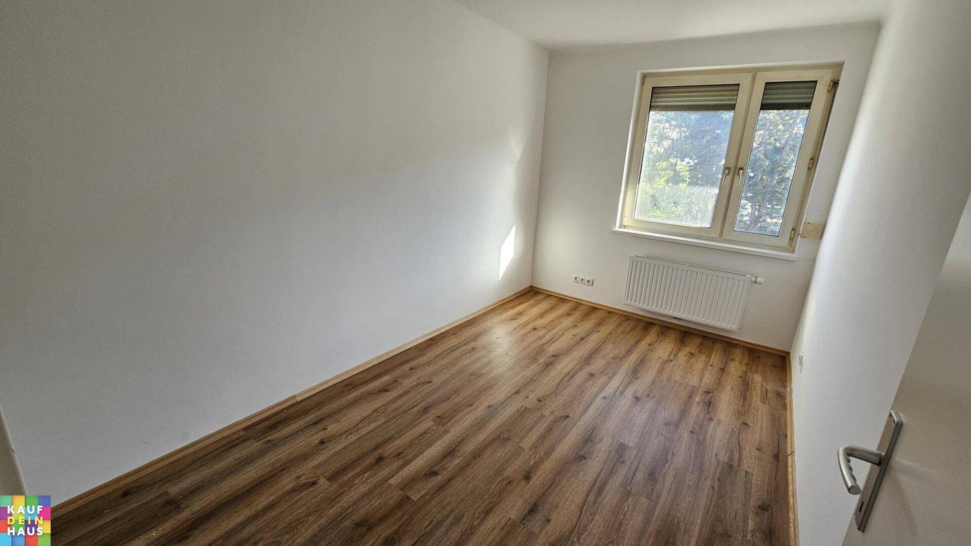 Weiteres Schlafzimmer mit Laminatboden und Fenster, ausgestattet mit Jalousien.