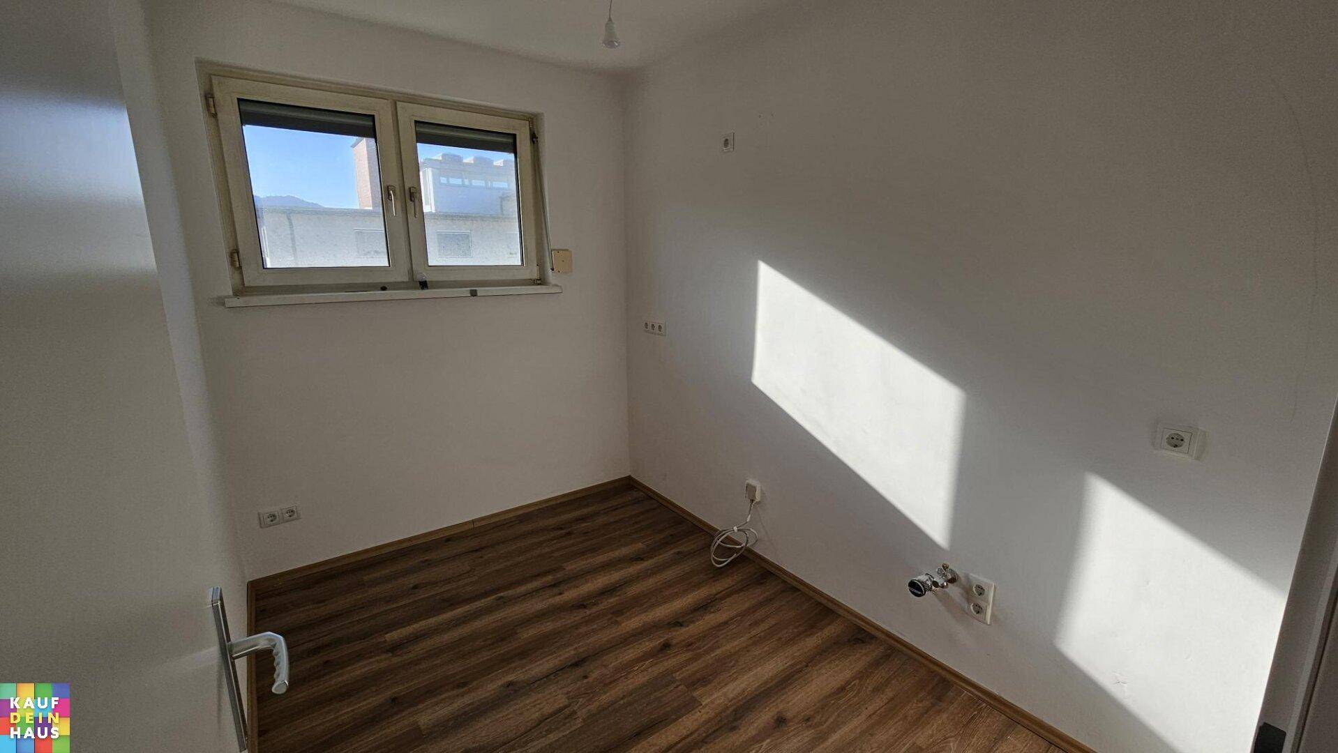Leerer Raum mit Laminatboden und Fenster, vorbereitet für die Installation einer Küche.