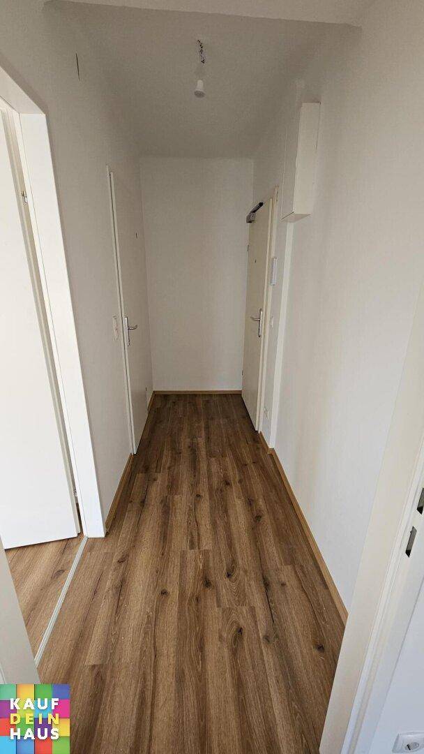 Langer Flur mit Laminatboden und weißen Wänden, der zu verschiedenen Zimmern führt.