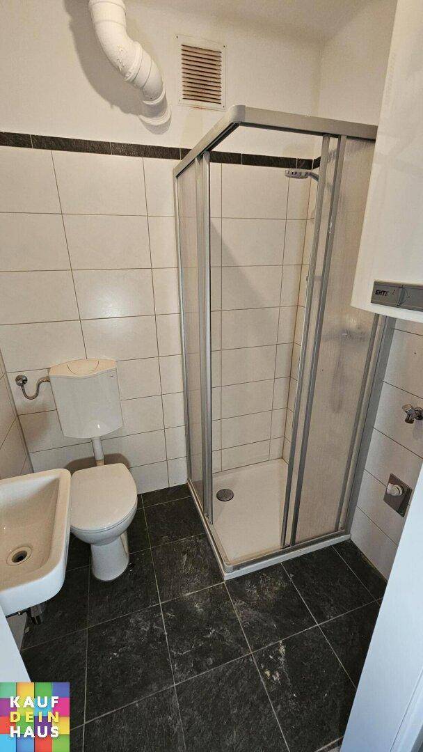 Kleines Badezimmer mit Duschkabine, WC, Waschbecken und Fliesen an Wänden und Boden.