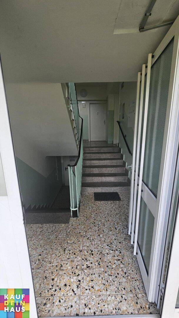 Eingangsbereich eines Mehrfamilienhauses mit Terrazzoboden und Treppenaufgang.