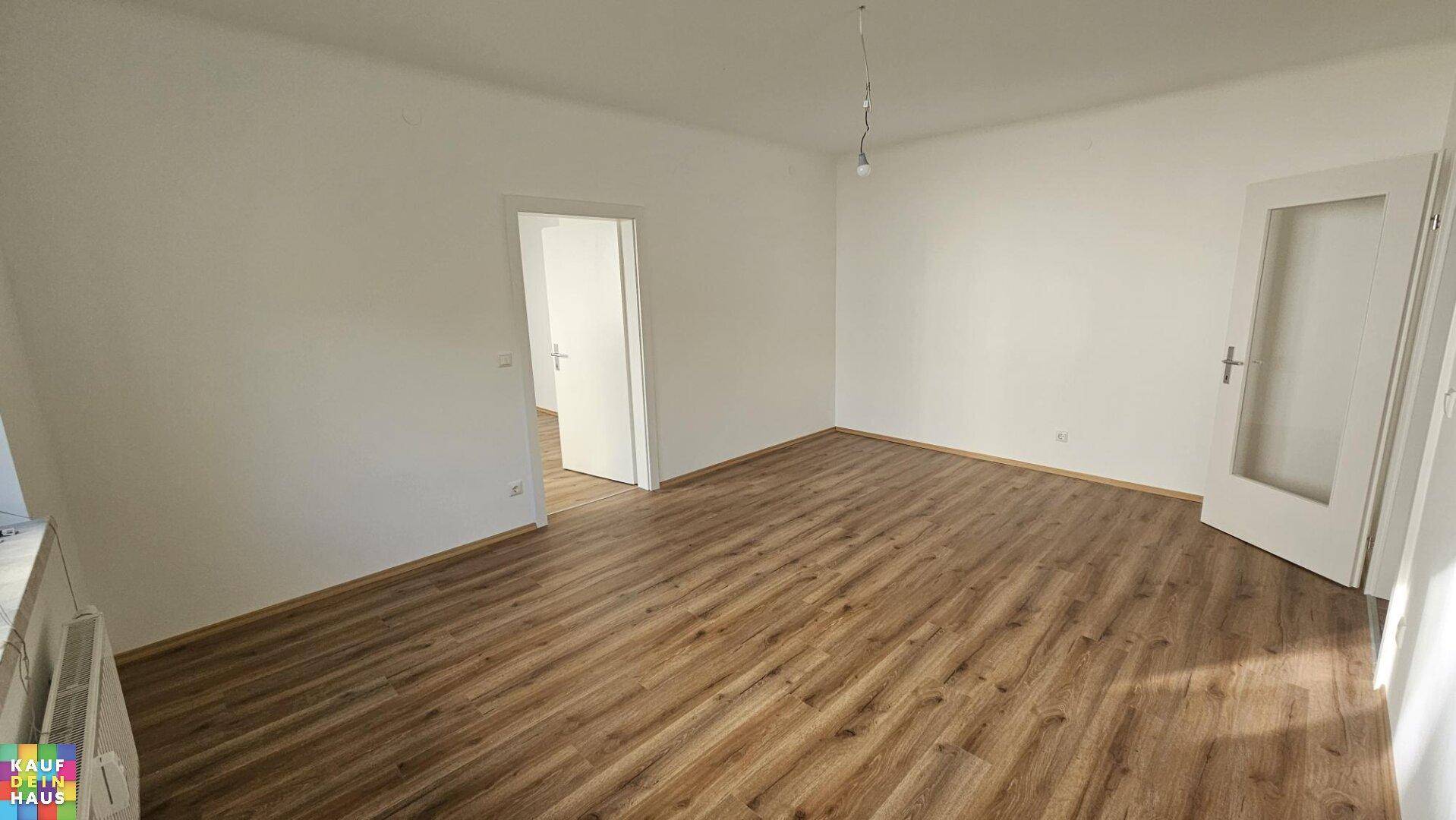 Geräumiges, leeres Zimmer mit Laminatboden und hellen Wänden, bereit zur individuellen Gestaltung.