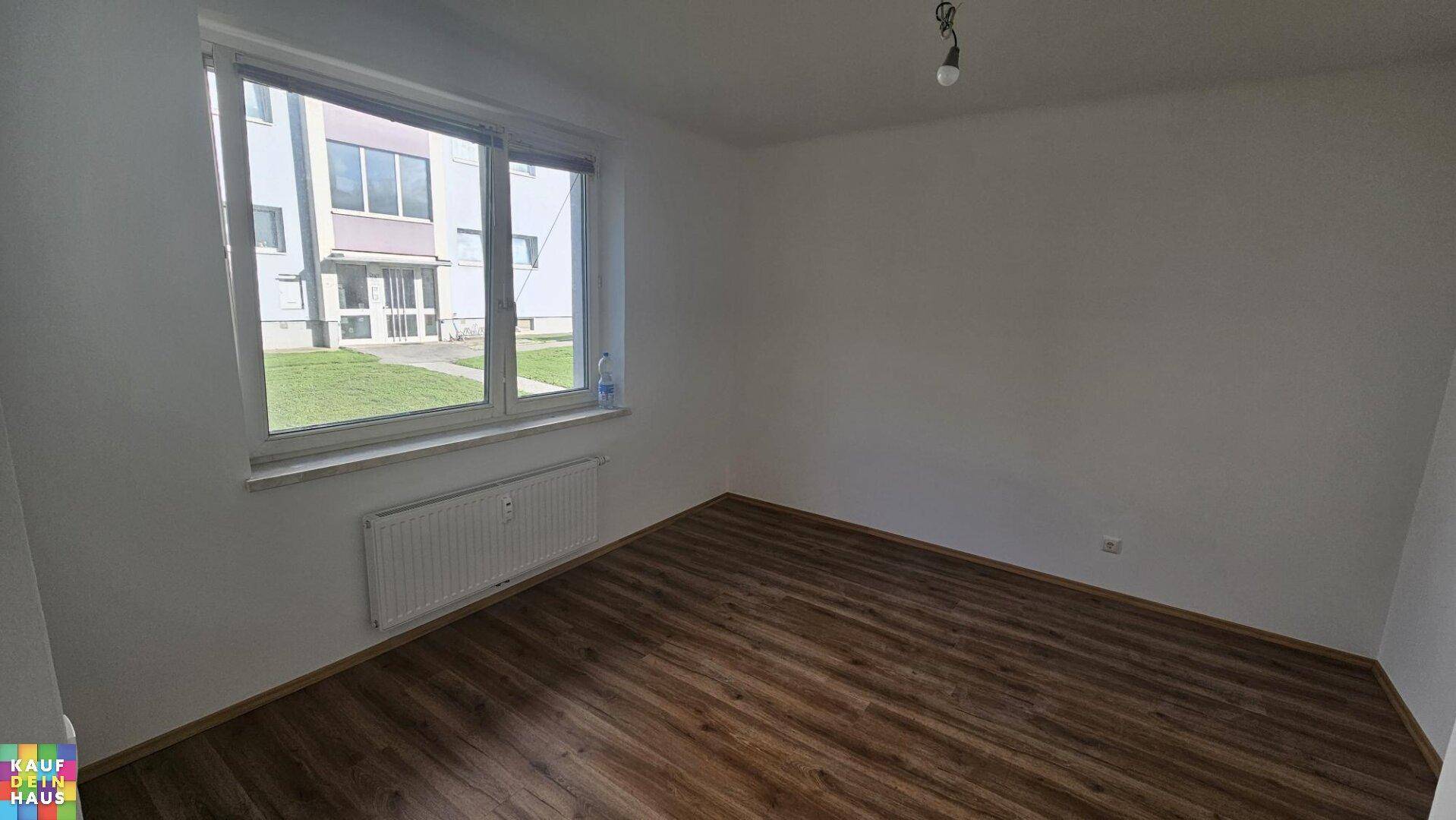 Helles Schlafzimmer mit Laminatboden, weiß gestrichenen Wänden und Blick auf den Innenhof.
