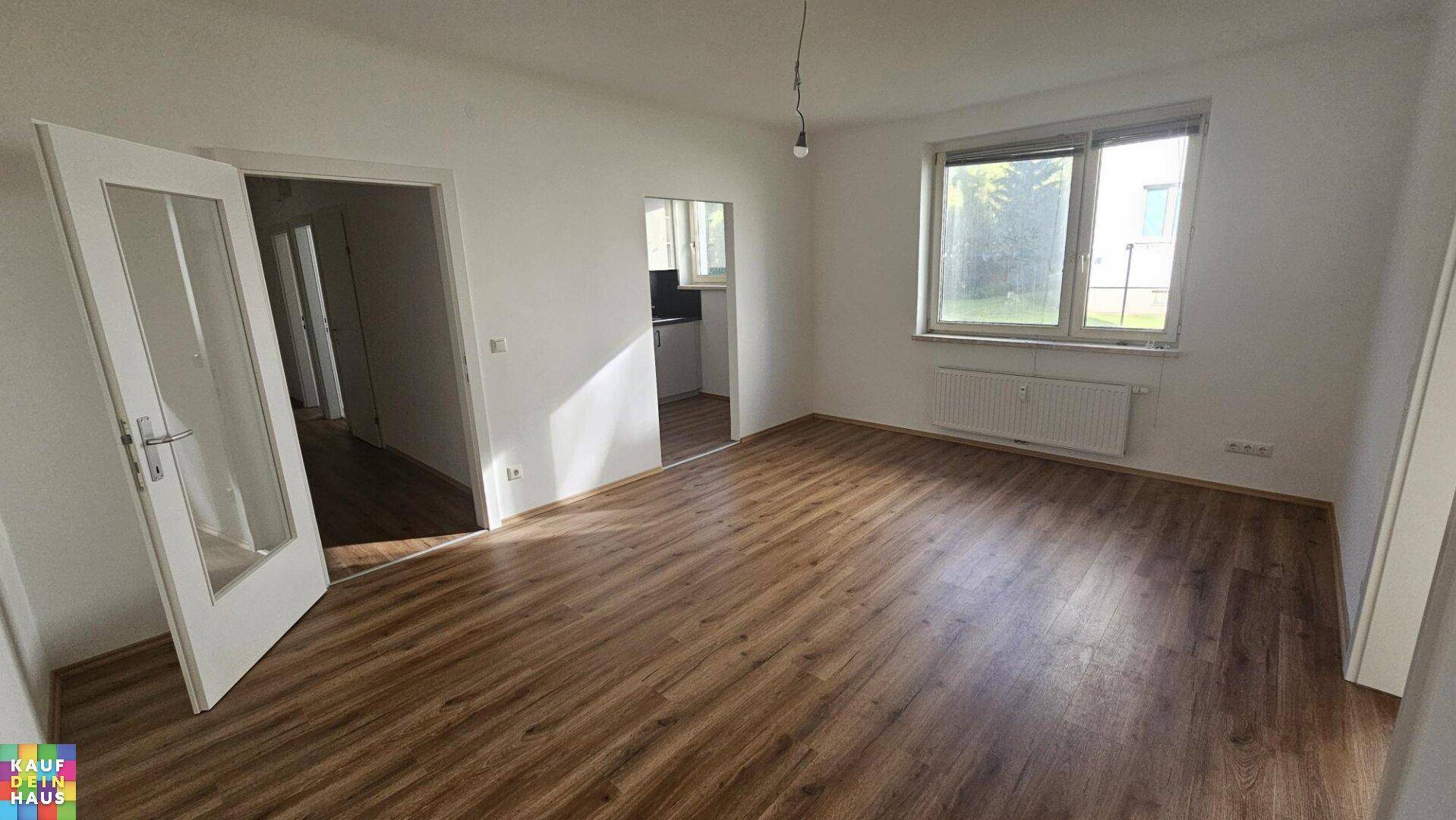 Heller Wohnraum mit neuem Laminatboden, weißen Wänden und Zugang zu weiteren Zimmern.