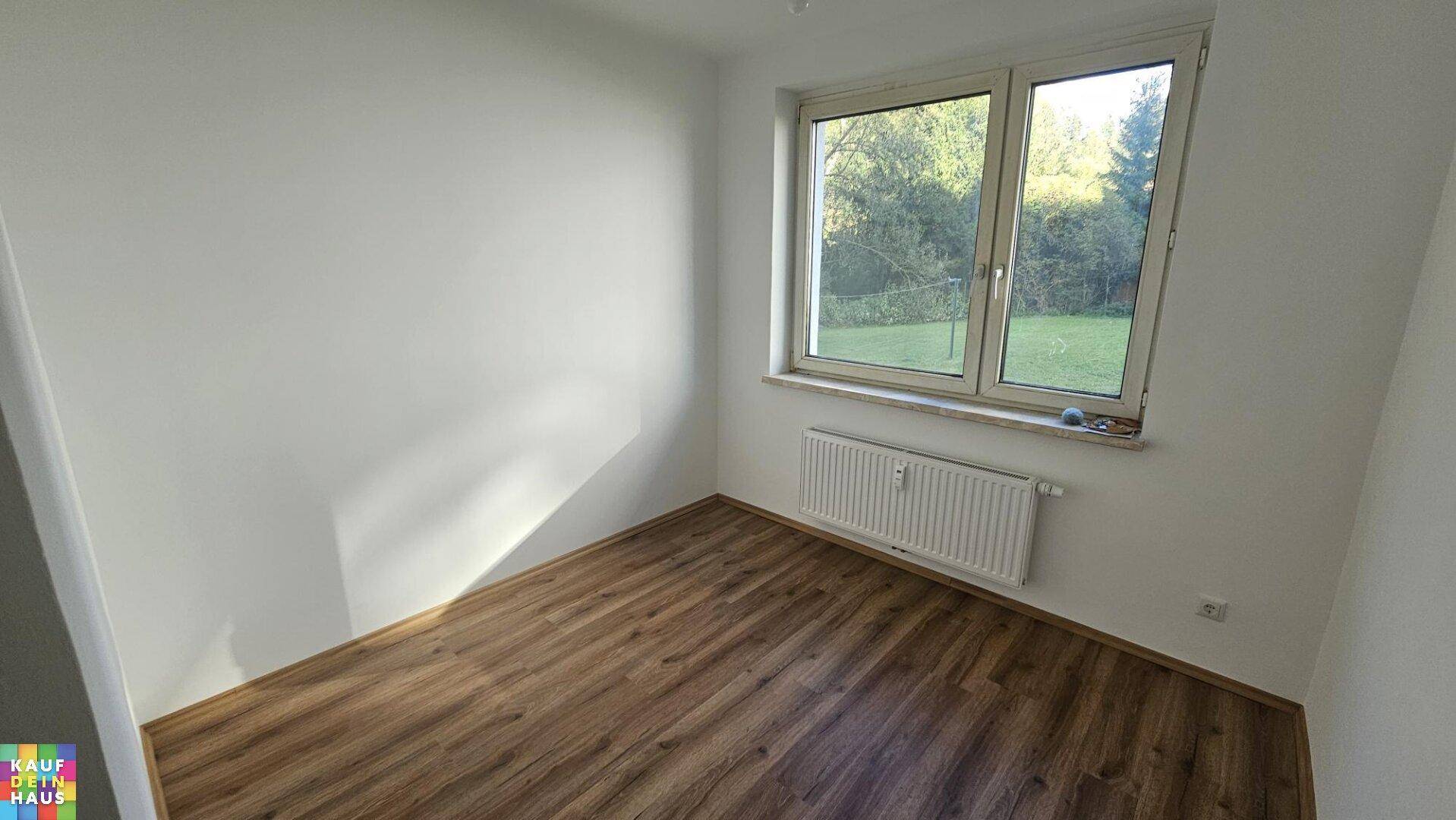 Freundliches Zimmer mit Laminatboden und Fenster mit Blick ins Grüne.