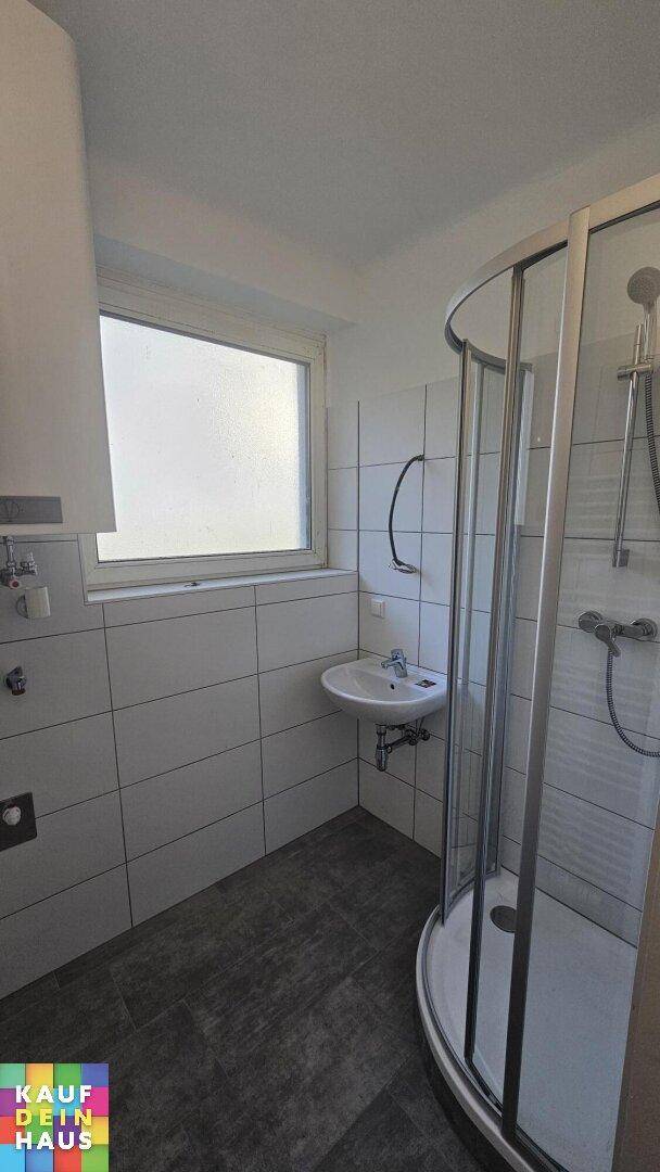 Modernes Badezimmer mit Duschkabine, Waschbecken, Fenster und hellen Fliesen.