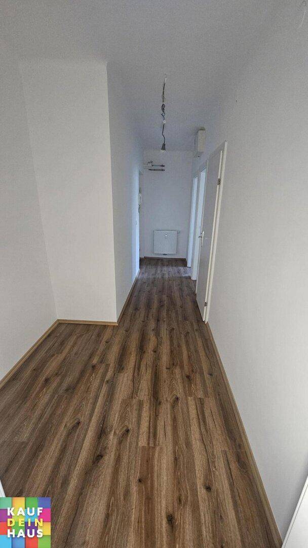 Langer, heller Flur mit neuem Laminatboden und weißen Wänden.