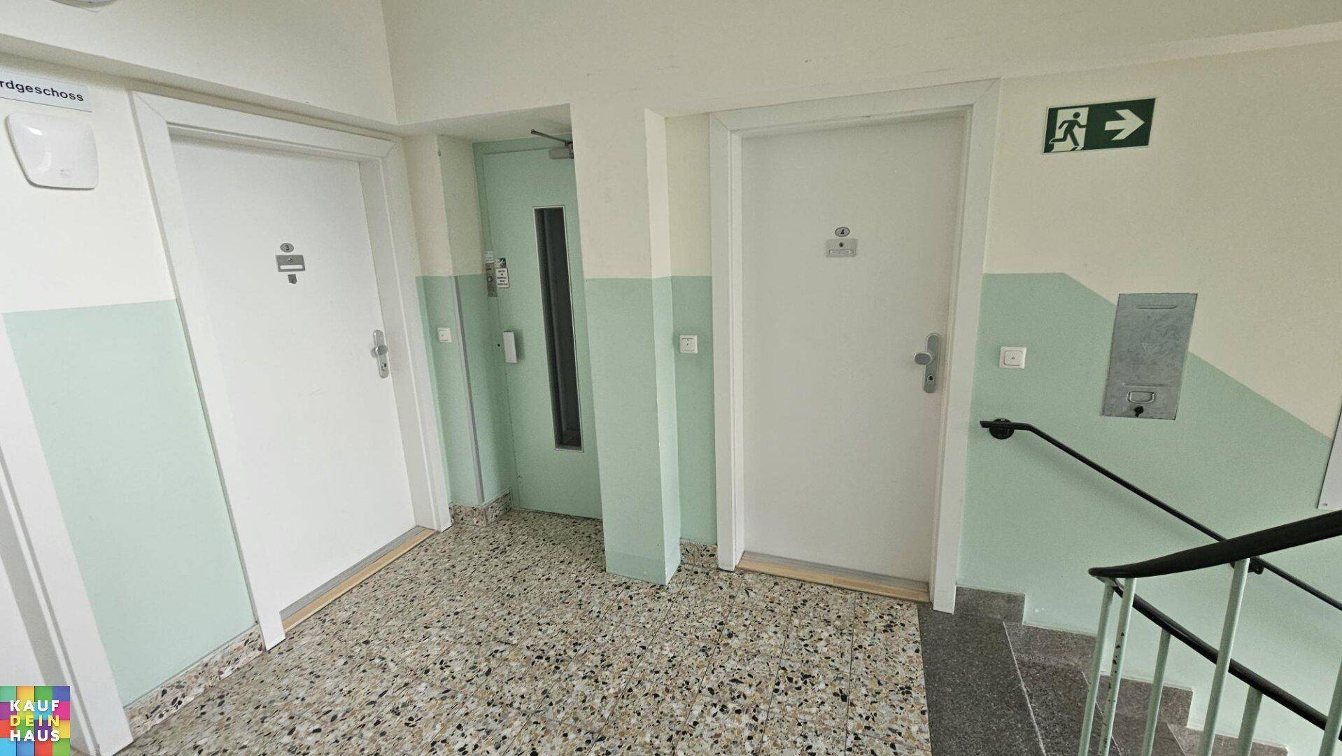 Gemeinschaftlicher Flur mit Aufzug, Treppenhaus und Terrazzoboden im Mehrfamilienhaus.