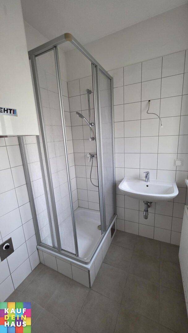 Funktionales Badezimmer mit Duschkabine, Waschbecken und weißen Fliesen, in gutem Zustand.