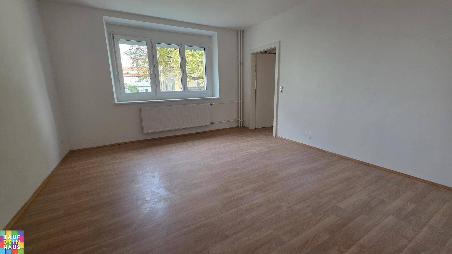 Heller Wohnraum mit Laminatboden, großen Fenstern und Heizkörper, bietet viel Gestaltungspotenzial.